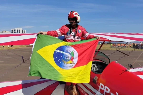 Imagem colorida mostra o piloto de avião Igor Reis, um homem branco vestindo um macacão vermelho e segurando uma bandeira metade do brasil, metade do Rio Grande do Sul - Metrópoles