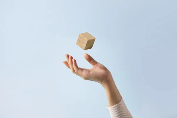 Foto mostra mão se preparando para segurar um cubo de madeira que lançou para o alto