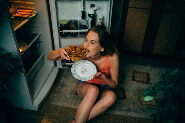 Foto mostra mulher comendo pizza direto de uma geladeira magros