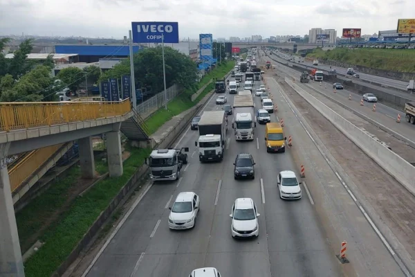 Imagem colorida mostra rodovoa com cinco faixas de carros circulando. No canto esquerdo há uma passarela com grades amarelas no acostamento da rodovia - Metrópoles