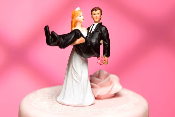 Foto colorida de bonecos de topo de bolo de casamento em um fundo cor-de-rosa - Metrópoles