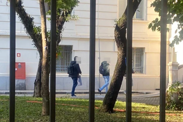 Imagem colorida mostra dois homem caminhando na área externa de prédio do IML - Metrópoles