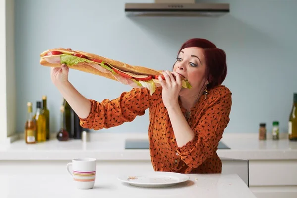 Mulher comendo um grande sanduiche- Metrópoles, calorias