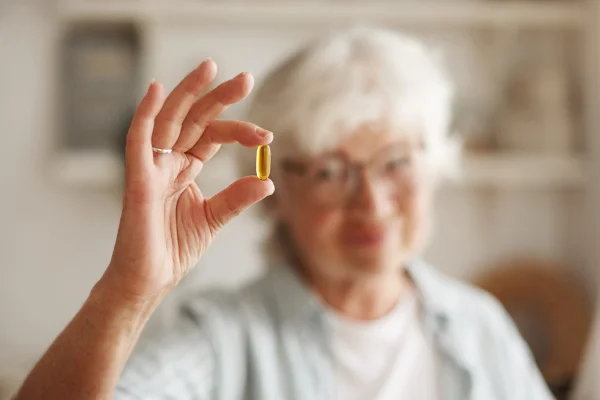 Imagem de uma idosa segurando uma pílula de vitamina b12 - Metrópoles