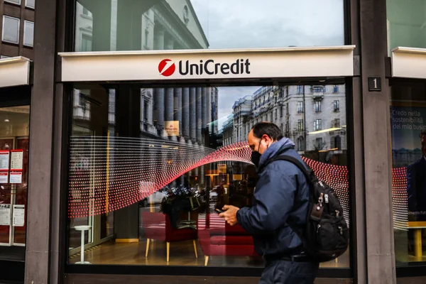 Homem de máscara passa em frente à fachada de um prédio com o logotipo do banco Unicredit - Metrópoles
