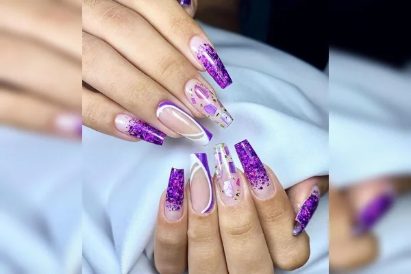 Unhas feitas por Raphael, ex-militar, em seu salão de unhas. Elas são longas, seguem padrões diferentes e predominam o roxo, lilás e branco, algumas com glitter - Metrópoles