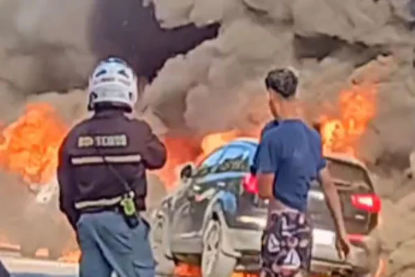Imagens coloridas mostram um agente do Corpo de Bombeiros e um jovem de camisa azul observando carros queimando, labaredas e fumaça preta de incêndio em São Paulo