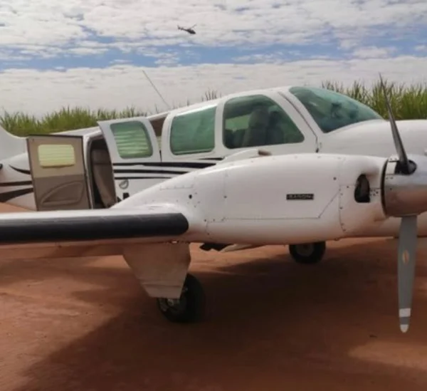 Imagem colorida do avião de prefixo PRPHM, que foi apreendido pela Polícia Federal com 400 kg de cocaína. A aeronave é branca com janelas de vidro verde e está pousada em uma pista de terra - Metrópoles