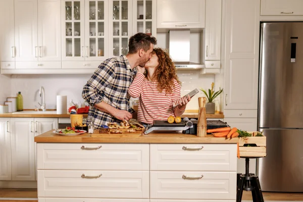 Foto colorida de casal de beijando na cozinha - Metrópoles