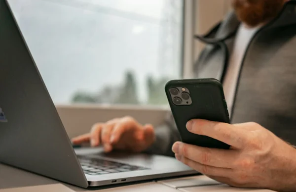Fotografia colorida mostrando homem segurando celular em frente ao computador-Metrópoles
