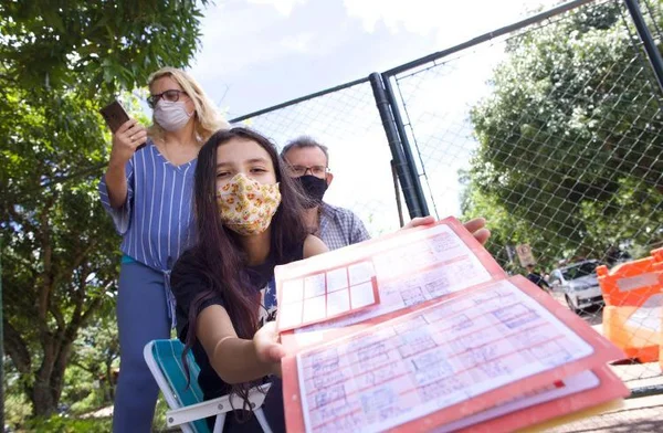 Menina de máscara mostrando cartões de vacina e pais atrás