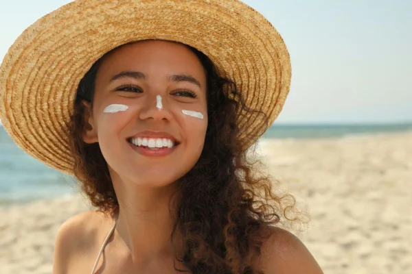 mulher usando protetor no rosto no sol na praia com chapeu