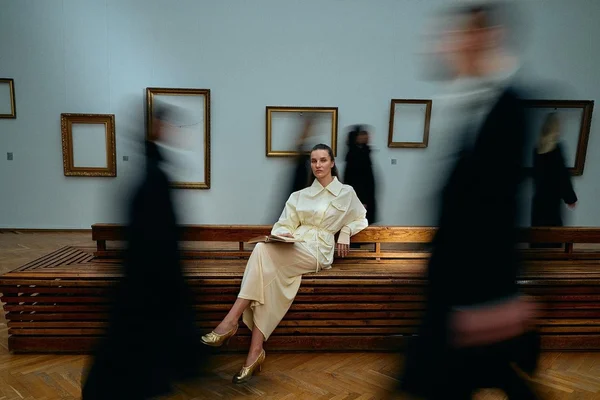 Campanha da marca ucraniana Kachorovska. Na imagem, uma modelo branca e jovem, de cabelo liso loiro escuro, posa sentada em um banco no Museu Nacional da Ucrânia. A parede mostra apenas a moldura de obras de arte que foram guardadas por causa do conflito. - Metrópoles