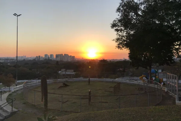 Imagem colorida da Praça Pôr do Sol. Foto mostra o horizonte, com o sol se podo no fundo, visto da perspectiva da praça