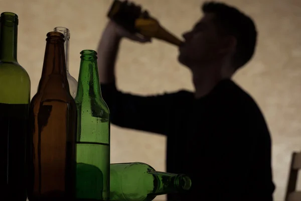 Foto colorida de garrafas de álcool, com sobrando masculina no fundo - Metrópoles.