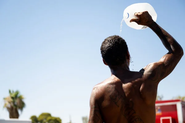Imagem colorida de homem negro molhando corpo com água durante onda de calor em Phoenix, Arizona, EUA - Metrópoles