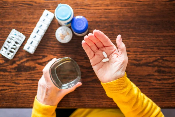 Foto colorida, mão feminina vestida com roupa amarela segurando medicamentos na mão - Metrópoles.