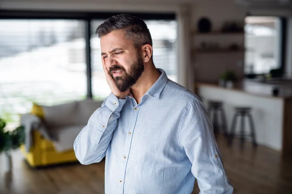 Imagem mostra homem de camisa social com a mão no rosto, representando dor de dente - Metrópoles