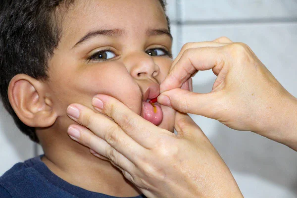 Foto colorida de criança tomando uma pílula laranja