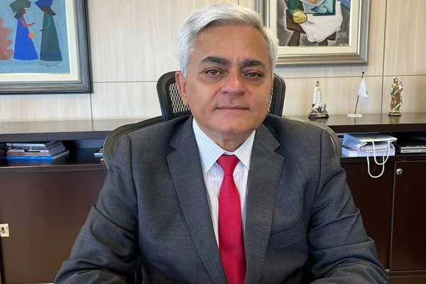 Fotografia colorida de homem com cabelo grisalho vestido de terno sentado à mesa