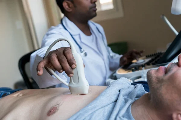 Indian doctor doing a heart ultrasound to a middle aged male patient at the hospital