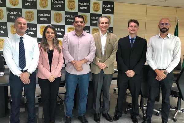 Homens e uma mulher ao lado um do outro em frente a painel da PCDF