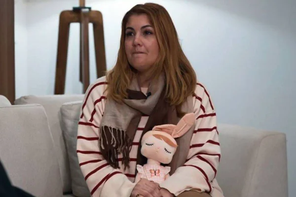 foto colorida de mulher de cabelos claros médios vestida em blusa listrada com boneca de pano no colo - metrópoles