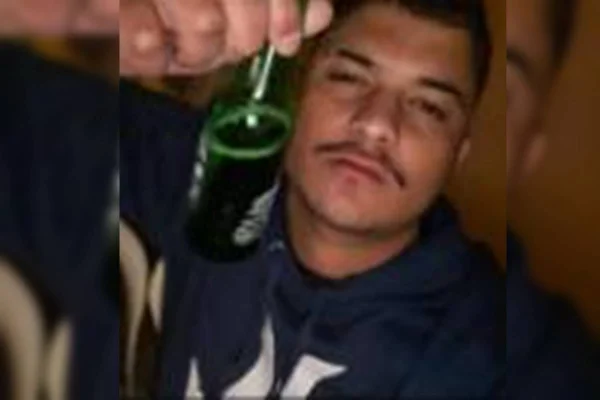 Jovem de camiseta azul marinho segurando cerveja longneck de garrafa verde - Metrópoles