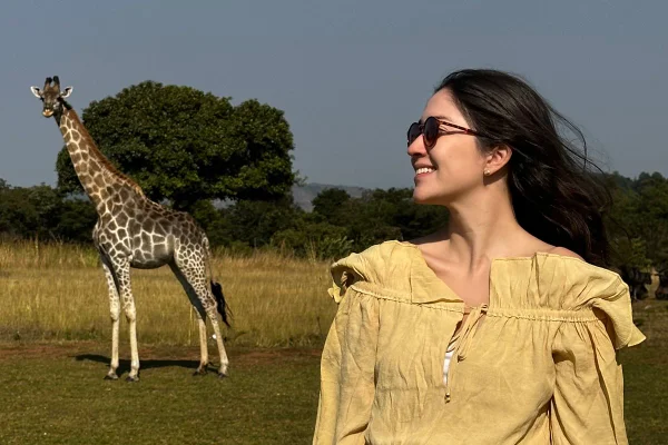 Foto colorida de mulher tirando foto perto de uma girafa - Metrópoles
