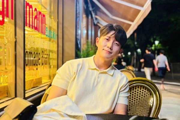 Imagem colorida do ator Park Min-jae usando blusa branca de gola polo, sentado em restaurante - Metrópoles