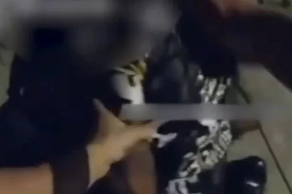 Imagem colorida de policial apontando arma na cabeça de um homem no chão. Metrópoles