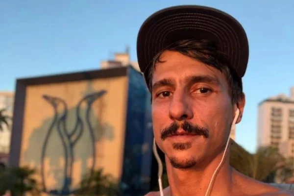 Gustavo Fildzz em foto colorida, de boné, sem camisa, fone de ouvido, de bigode