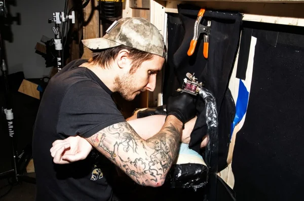 Scott Campbell apresenta projeto “Whole Glory” onde pessoas colocam o braço dentro de um buraco e, sem ver, saem tatuados
