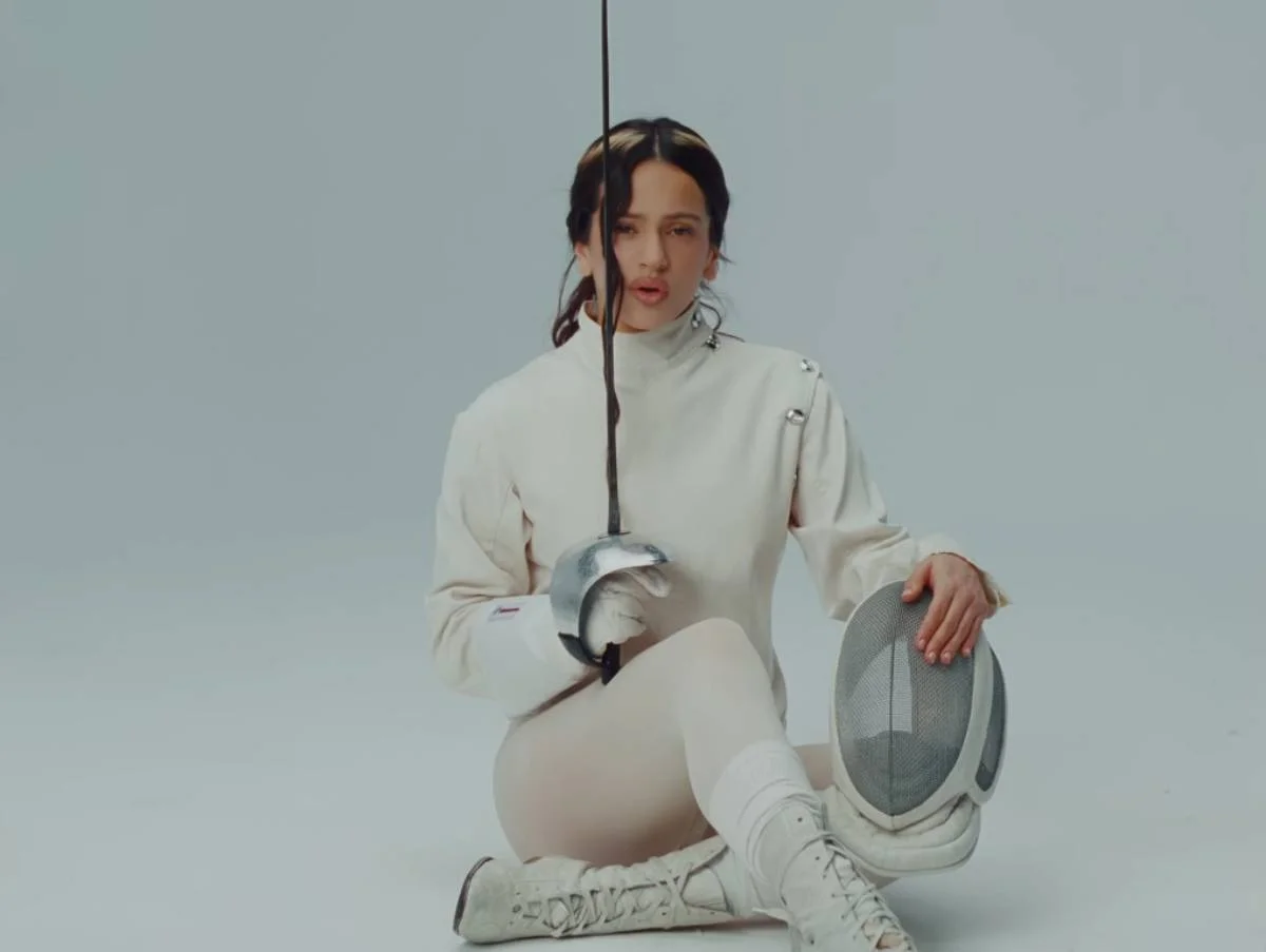 O clipe abre com uma cena da artista vestida com trajes de esgrima O clipe abre com uma cena da artista vestida com trajes de esgrima