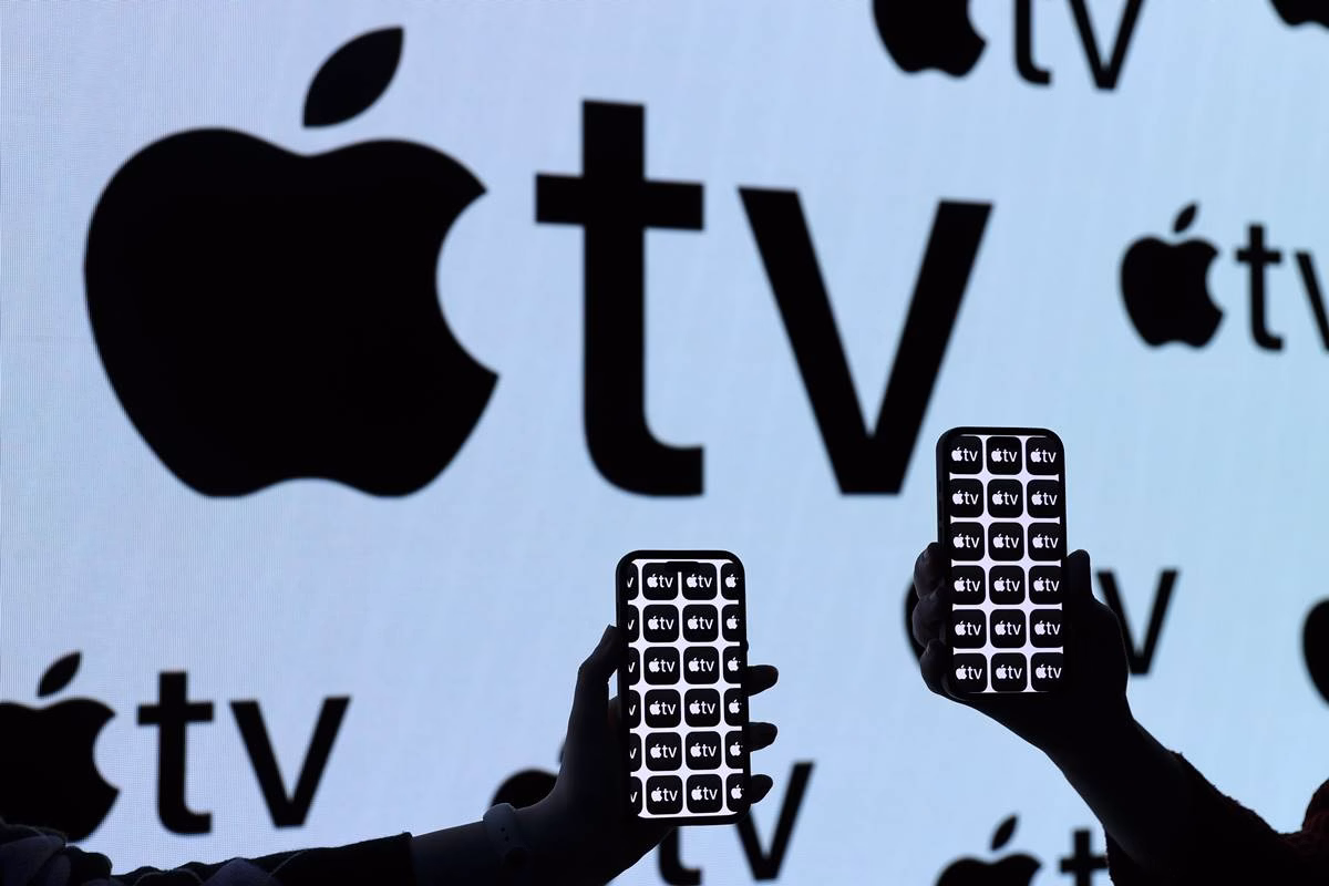 Painel led com o símbolo da apple tv e duas pessoas segurando um smartphone na frente - metrópoles