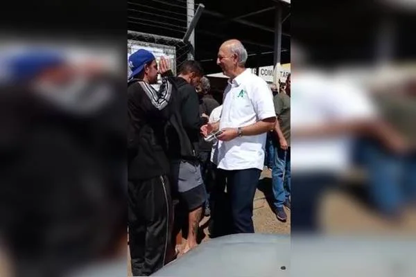 Imagem colorida de pessoas na fila e homem de camisa branco cumprimentando cidadãos