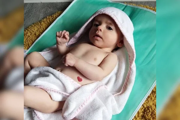 Recém nascida com toalha na cabeça deitada sobre manta verde e com manchade coração na barriga