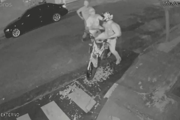 Imagens em preto e branco de uma câmera de segurança mostram um motociclista sendo abordado por dois homens armados com facas em uma rua - Metrópoles