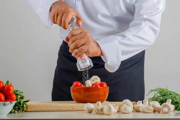 Homem de camisa branca coloca sal em salada com legumes - Metrópoles