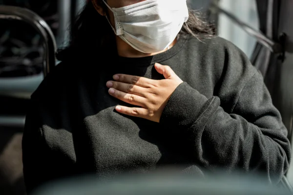 Foto colorida de mulher gripada, usando máscara e uma blusa de frio preta - Metrópoles