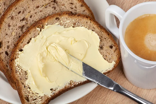 Foto colorida de manteiga em pão e, ao lado, xícara com café - Metrópoles