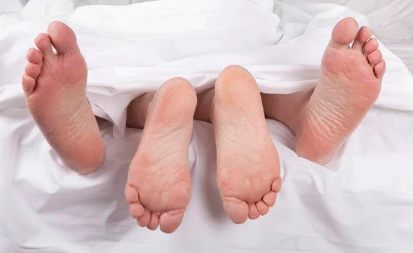 Pés entrelaçados embaixo do edredom
