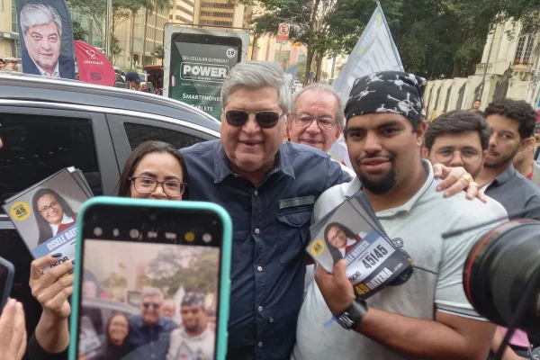 Imagem mostra homem de óculos escuro cercado por pessoa com bandana e mulher - Metrópoles