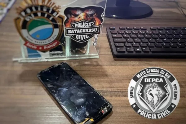 Imagem colorida, mesa de escritório, logo da Polícia e celular sobre a mesa - Metrópoles