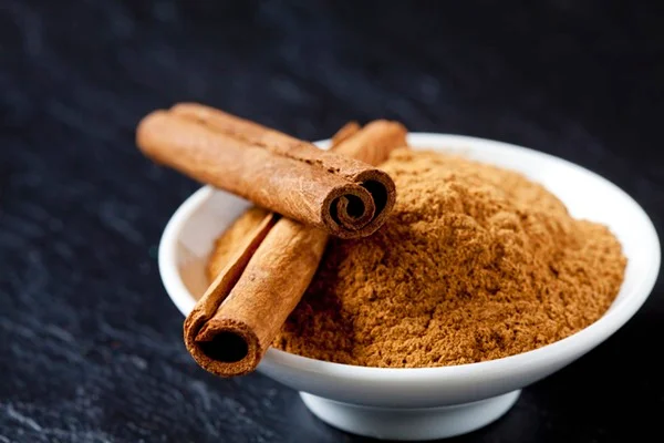 Um recipiente branco com canela em pó está em cima de uma superfície de madeira