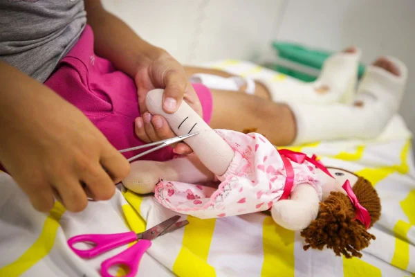 Foto de menina com tesoura cortando curativo da boneca - Metrópoles