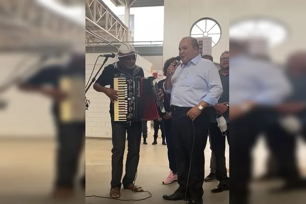 Homem segura sanfona ao lado de homem com microfone