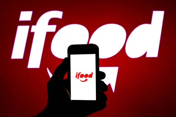 imagem colorida com logotipo do iFood e celular na mão de uma pessoa