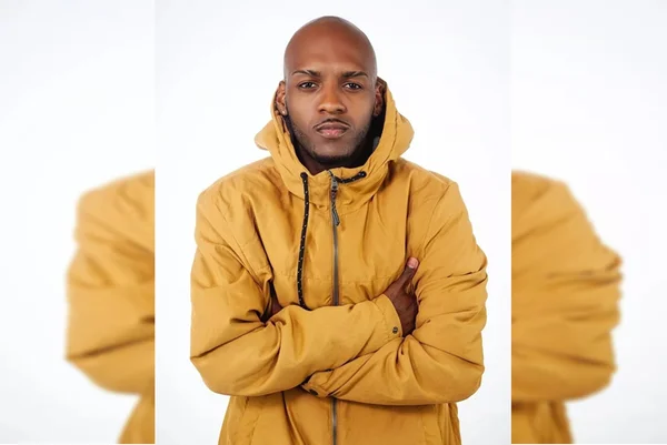 homem negro veste um casaco amarelo e posa para foto com os braços cruzados