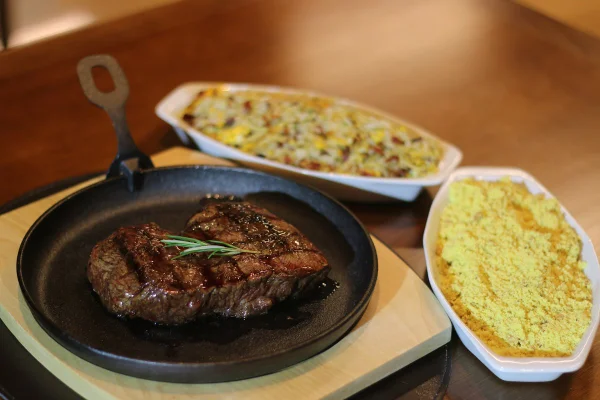 Panelinha com carnes e travessas com arroz e farofa